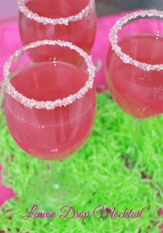 three glasses filled with pink liquid sitting on top of green moss