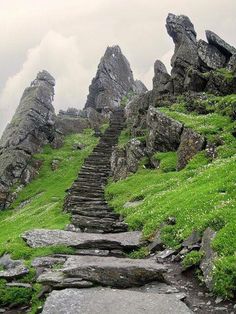 some rocks and green grass on the side of a steep hill with steps leading up to it