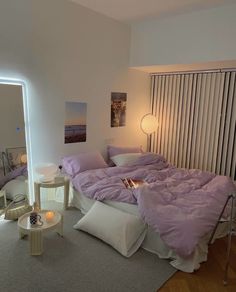 a bed with purple sheets and pillows in a room next to a wall mounted mirror