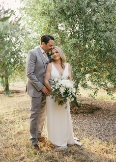 a bride and groom standing under an olive tree