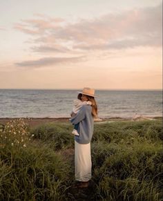 a woman wearing a hat standing in tall grass near the ocean