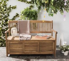 a wooden bench sitting in front of a wall covered with plants and potted plants