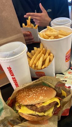 a hamburger and french fries are sitting on a table next to two cups of soda