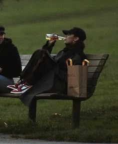 two people sitting on a park bench drinking sodas and eating food from paper bags