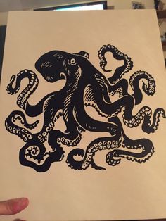 an octopus is depicted on a piece of paper in black ink with white background and hand holding it up