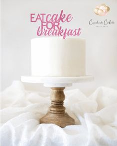 a white cake sitting on top of a wooden stand with the words eat cake for breakfast