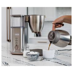 a person pouring coffee into a cup next to a blender on a counter top