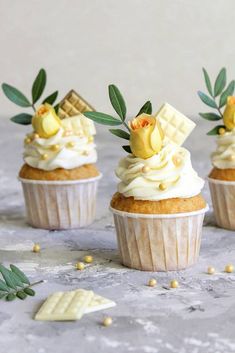 three cupcakes with white frosting and flowers on top