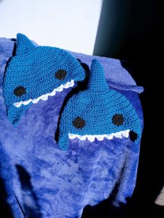 two crocheted shark hats sitting on top of a blue blanket