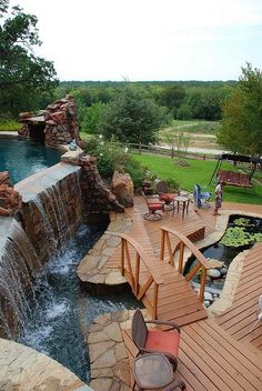 a wooden deck next to a pool with water flowing from it and people standing on the other side