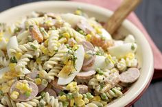 a white bowl filled with pasta and vegetables next to a wooden spoon on top of a table