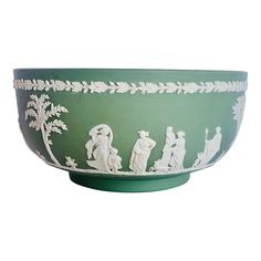 a green bowl with white designs on the side and people in trees painted on it