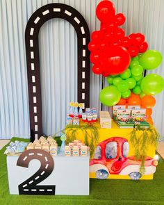 a table topped with balloons next to a number two sign and race car cake stand