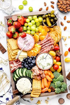 a platter filled with cheese, crackers, fruits and vegetables next to nuts