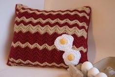 a crocheted pillow with two eggs sitting on top of it next to an egg carton