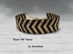 a close up of a bracelet on a white surface with black and gold strips in the middle