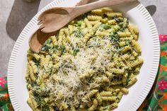 a white plate topped with pasta covered in parmesan cheese and spinach next to a wooden spoon