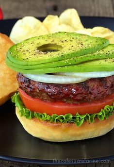 a hamburger with lettuce, tomato and onion on it next to some potato chips