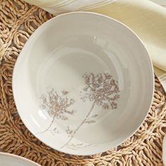 white dishes with brown designs on them sitting on woven placemats