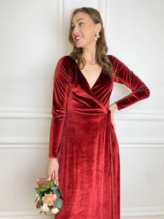 a woman in a red velvet dress holding a bouquet and posing for the camera with her hands on her hips