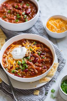 two bowls of chili with sour cream and tortilla crackers on the side