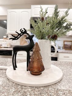 a vase with some plants in it sitting on a counter next to a deer figurine