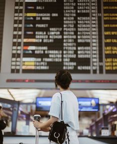 a woman standing at an airport with her luggage and looking at the departure board in the background