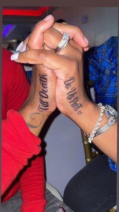 two people are holding hands with tattoos on their arms and the other hand has writing on it