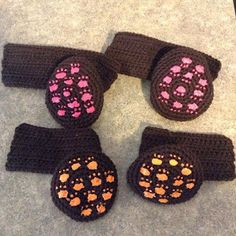 four crocheted dog paw mitts with pink and orange designs on them sitting on the floor