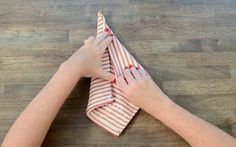 two hands on top of a wooden table holding a red and white striped towel