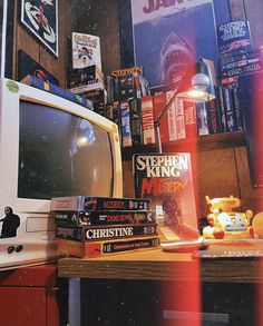 a television sitting on top of a wooden table next to a pile of books in front of a window