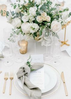 a table set with white and gold place settings, silverware, napkins and flowers