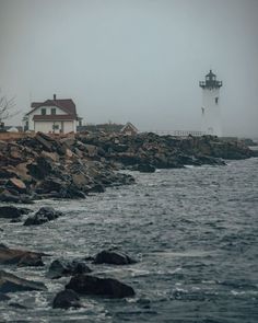 a light house on the shore with waves crashing in front of it and foggy sky