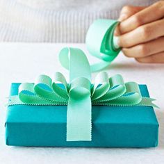 a person holding a green ribbon on top of a blue present box