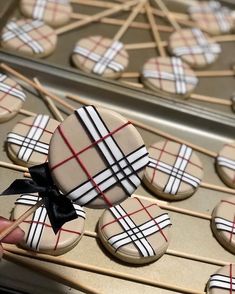 cookies decorated with plaid and black bows are being held by sticks on a baking sheet