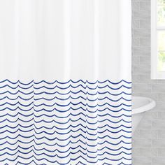 a white shower curtain with blue waves on it in a gray tiled bathtub next to a window