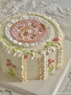 a white cake with pink frosting and flowers on the top is sitting on a lace doily