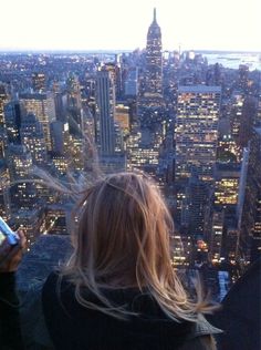 a woman standing on top of a tall building looking down at the city lights and skyscrapers