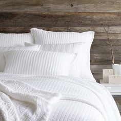 a bed with white sheets and pillows on top of it next to a wooden headboard