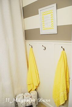 two yellow towels hanging on hooks in a bathroom with striped walls and white cabinetry