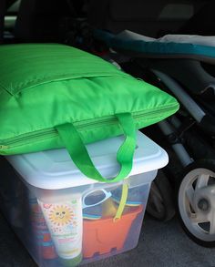 a green bag sitting on top of a plastic container next to a stroller