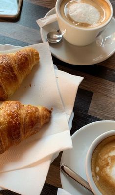 two croissants are sitting on napkins next to a cup of coffee