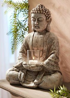 a buddha statue holding a candle on top of a table