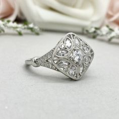 an antique style diamond ring sits next to a rose