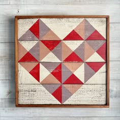 a wooden frame with some red and grey triangles on it, hanging on the wall