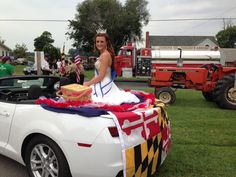 a woman sitting on top of a white car with an american flag draped over it