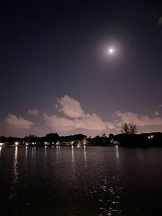 the moon is shining brightly in the night sky over water with houses and trees on either side