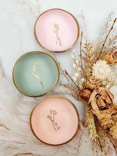 three plates with designs on them sitting next to dried flowers