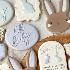 decorated cookies with bunny ears and bunnies are on a wooden plate next to the cookie saying oh baby, she's for me what will our bunny be?