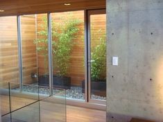 the inside of a house with glass walls and wooden flooring, plants on either side